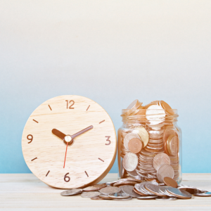 A clock next to a bunch of coins in a glass.